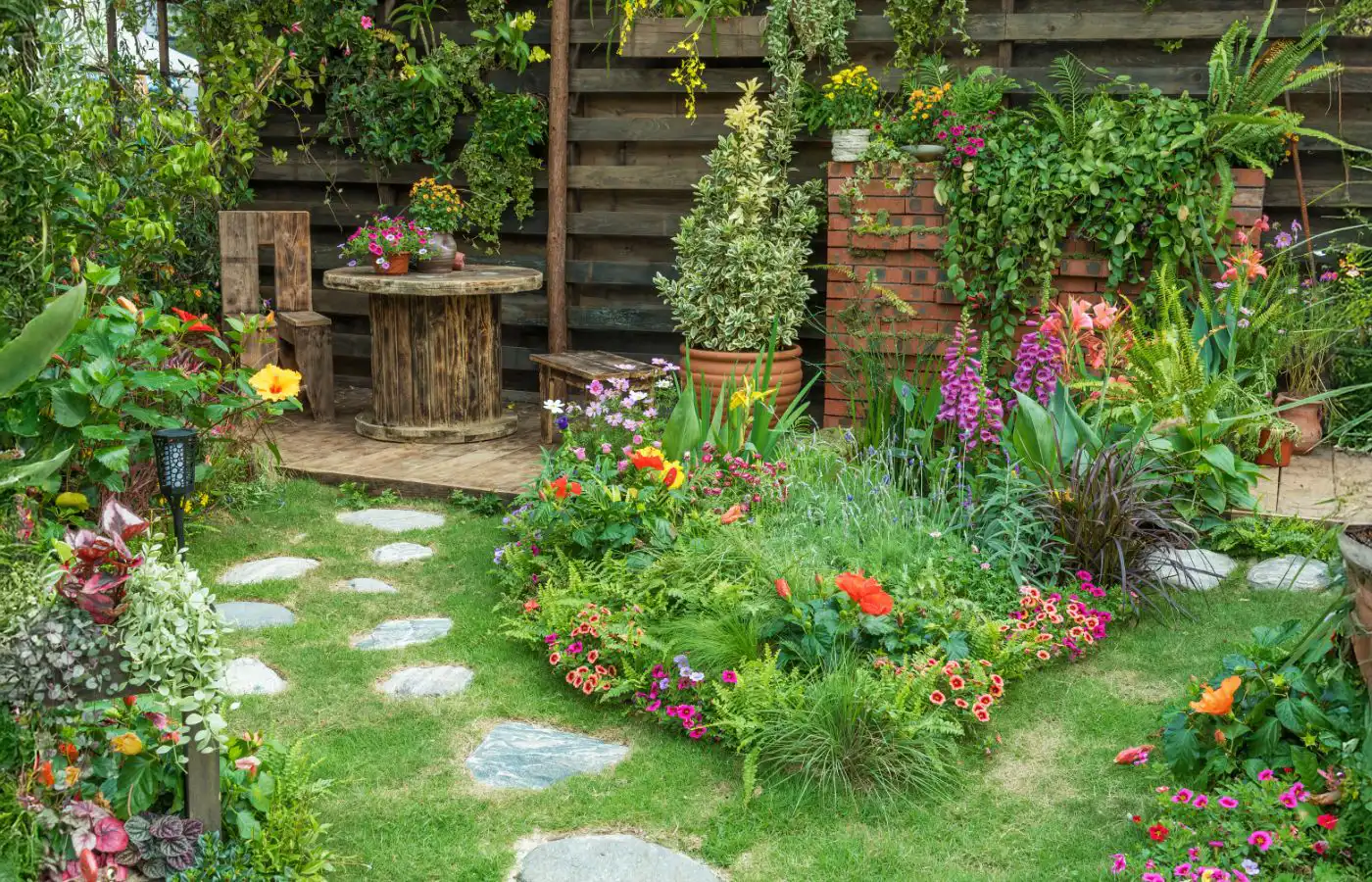 Jardin aménagé avec des fleurs colorées, un chemin de galets, et un coin salon en bois, créant une ambiance chaleureuse et naturelle.