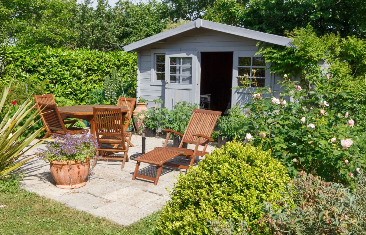 Coin de jardin avec mobilier en bois et cabane, entouré de plantes et de fleurs, créant un espace de détente convivial et naturel.