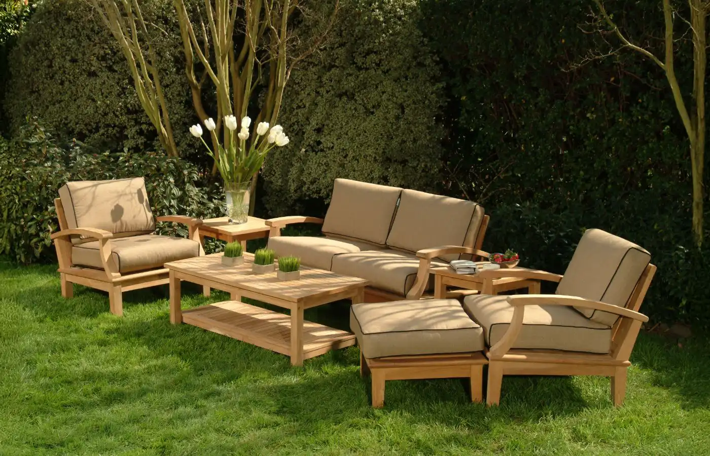 Salon extérieur aménagé avec des meubles en bois et des coussins beige, dans un jardin verdoyant, créant un espace convivial et relaxant.